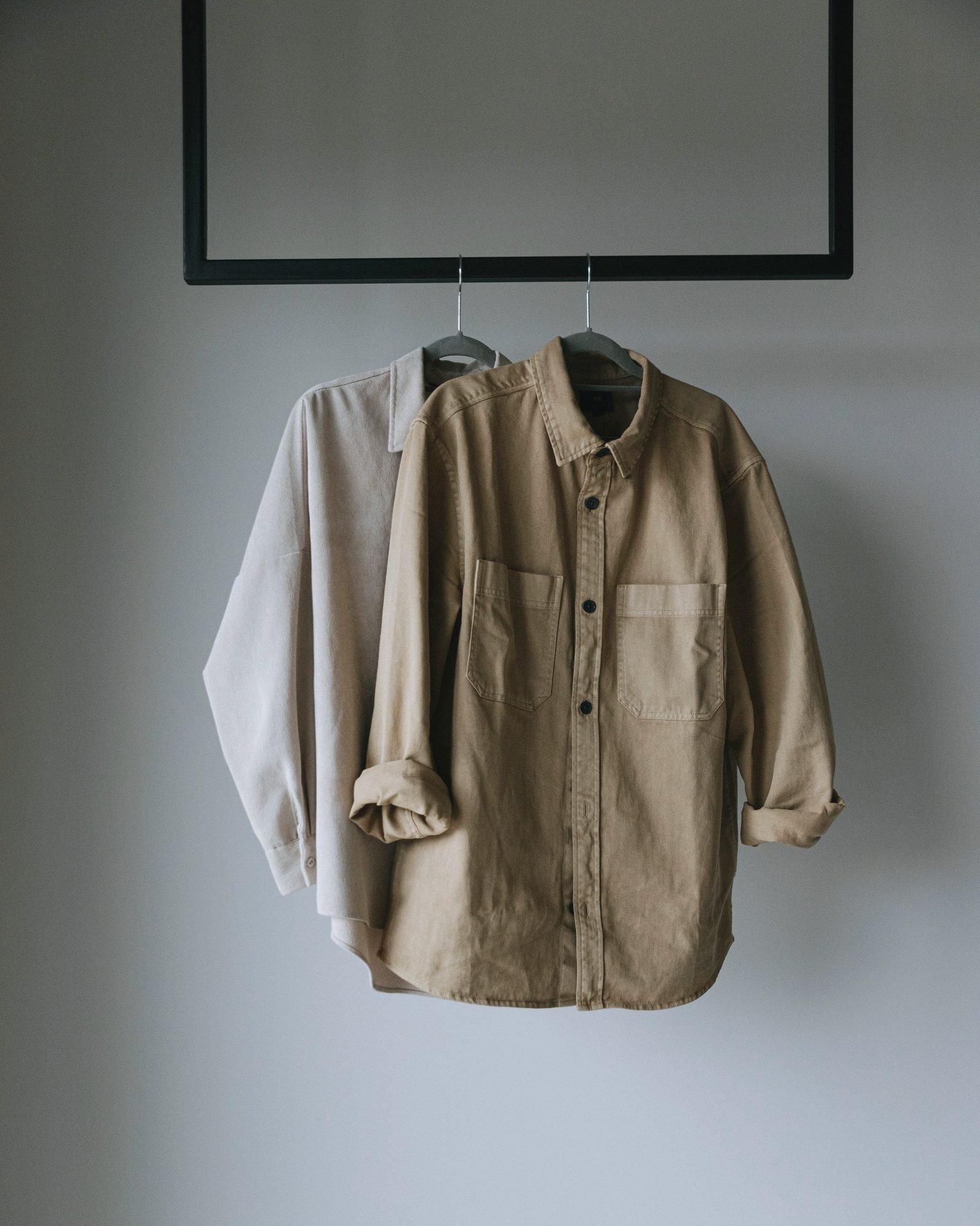 Two plain work shirts on hangers against a bare wall