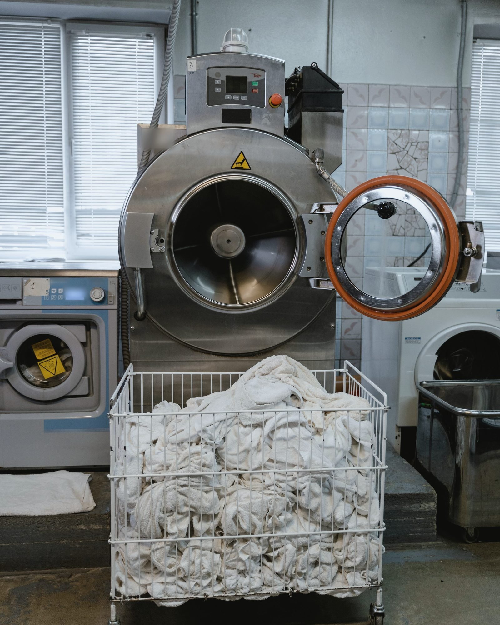 Industrial washer standing open above a cart of white linens